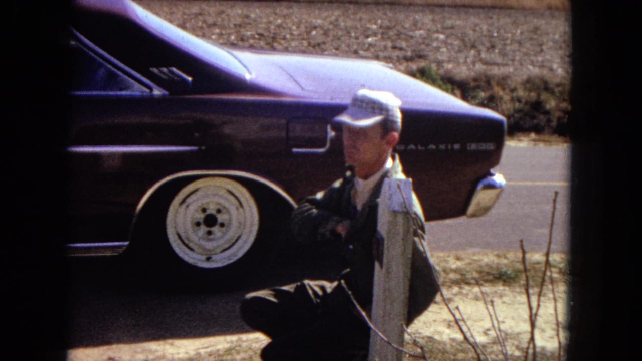 A man in a checkered cap squats near the rear of a purple car.