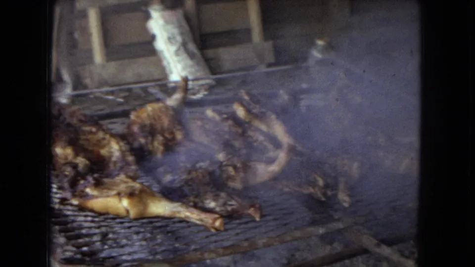 Whole chickens roast over smoky coals on a metal grill in 1967 8mm home-movie footage from the United States.