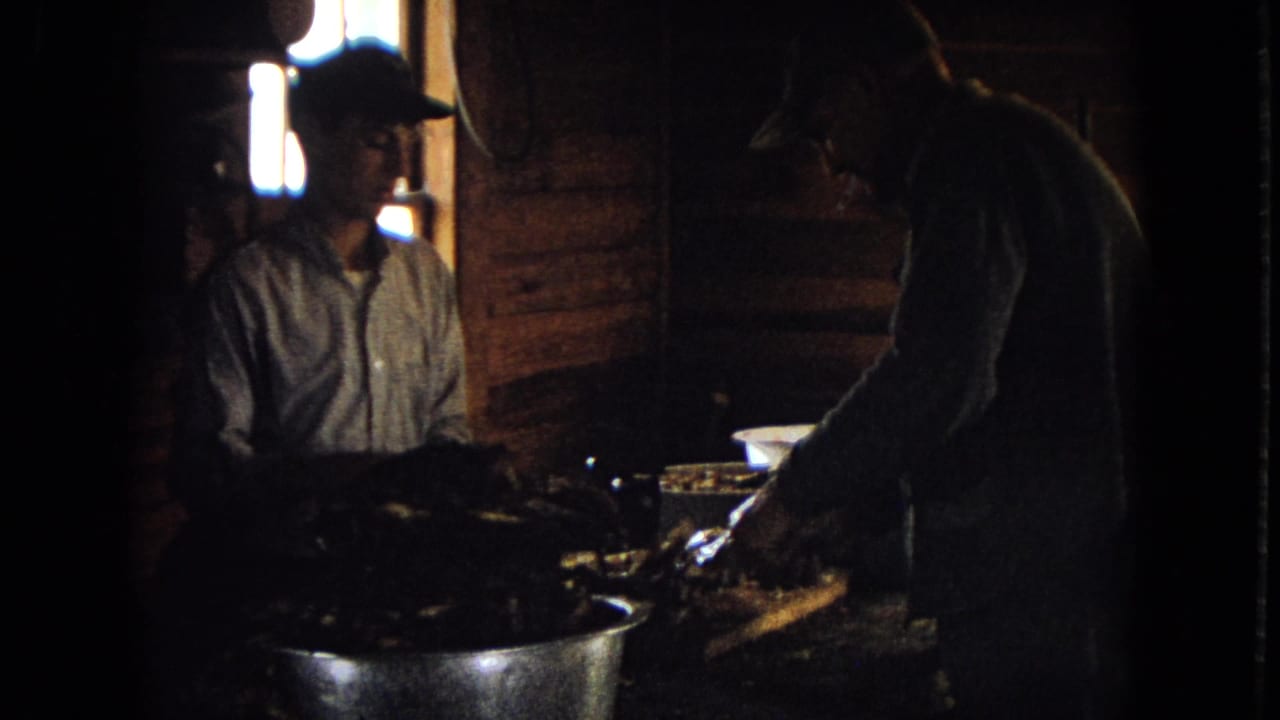 Two men work at a table inside a dark wooden cabin.