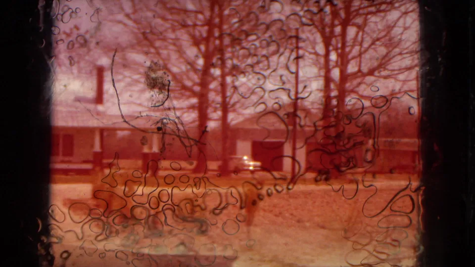 A red-tinted damaged or exposed section of 8mm film overlays the farmhouse, driveway, trees, and parked car, creating a visible archival film artifact.
