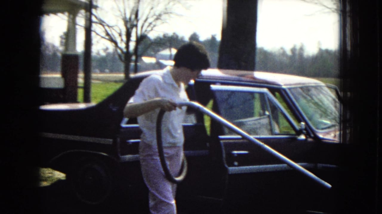 Woman stands next to a dark car holding a vacuum hose and long wand.