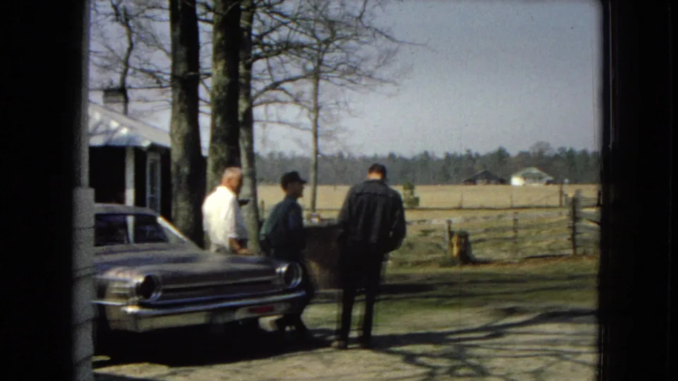 A doorway-framed 8mm view shows three adult men by a classic sedan in a rural setting associated with the supplied 1967 metadata.
