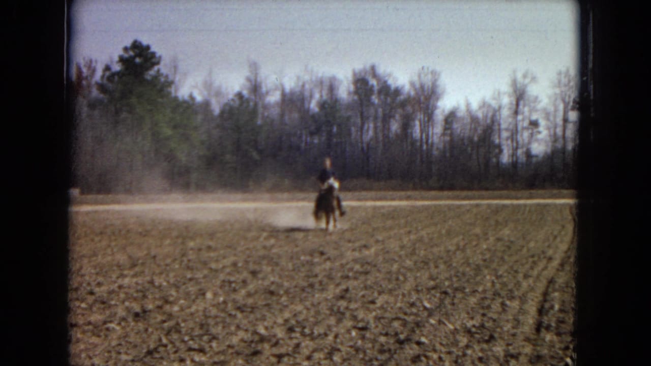 A distant rider on a small pony moves across a dusty plowed field in 1967 Arizona home-movie footage, with bare trees lining the background.