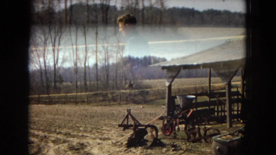 The final frame shifts away from the rider toward farm equipment near fencing, bare trees, open fields, and the edge of a weathered barn or shed roof.