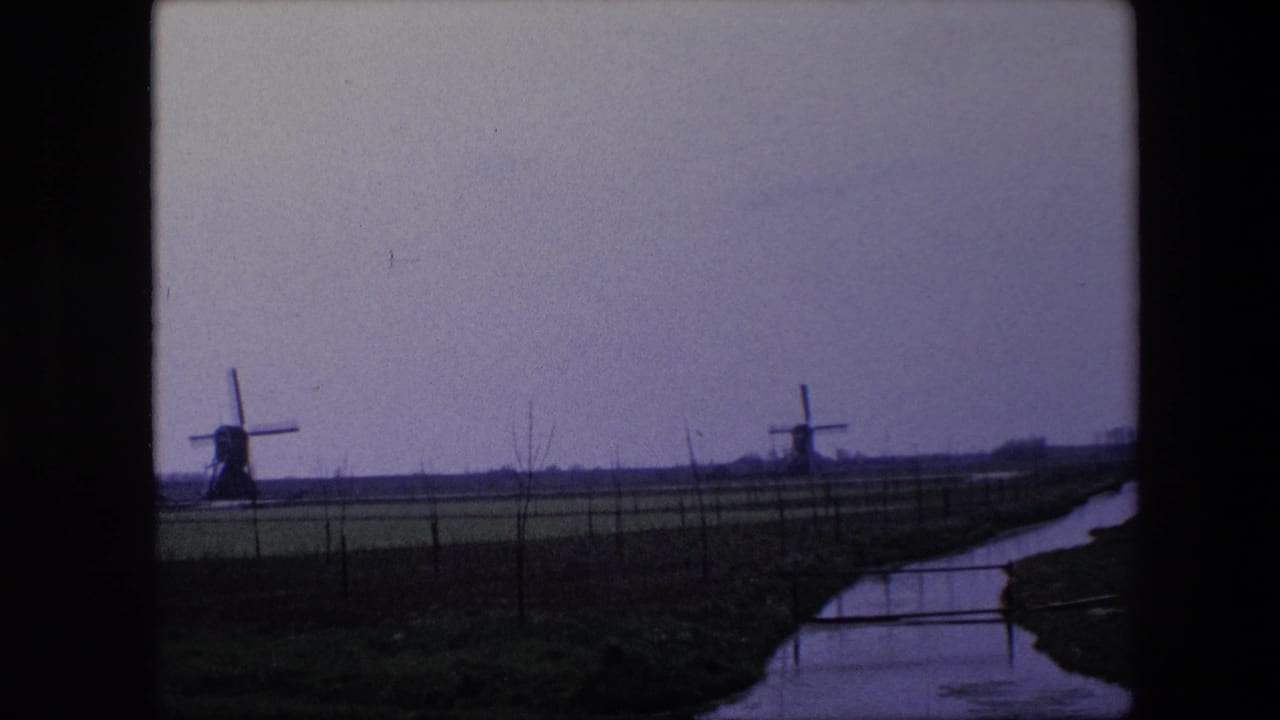 Flat rural field with two windmills, fencing, and a waterway running along the right edge.