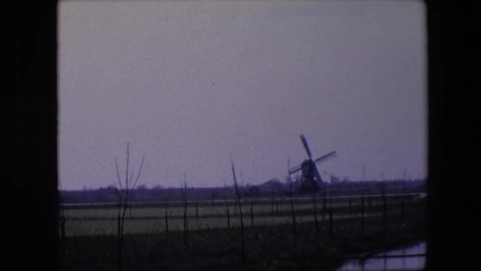 8mm frame from 1967 near Brussels showing a distant windmill, low agricultural fields, sparse trees, and dark window or vehicle framing.