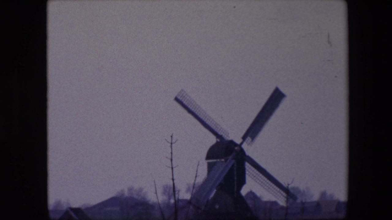 1967 8mm frame from Brussels, Belgium, with the windmill filling more of the view, its sails angled across a pale sky and low buildings receding behind it.