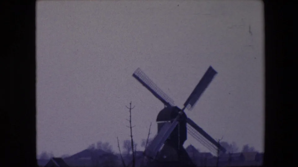 1967 8mm frame from Brussels, Belgium, with the windmill filling more of the view, its sails angled across a pale sky and low buildings receding behind it.
