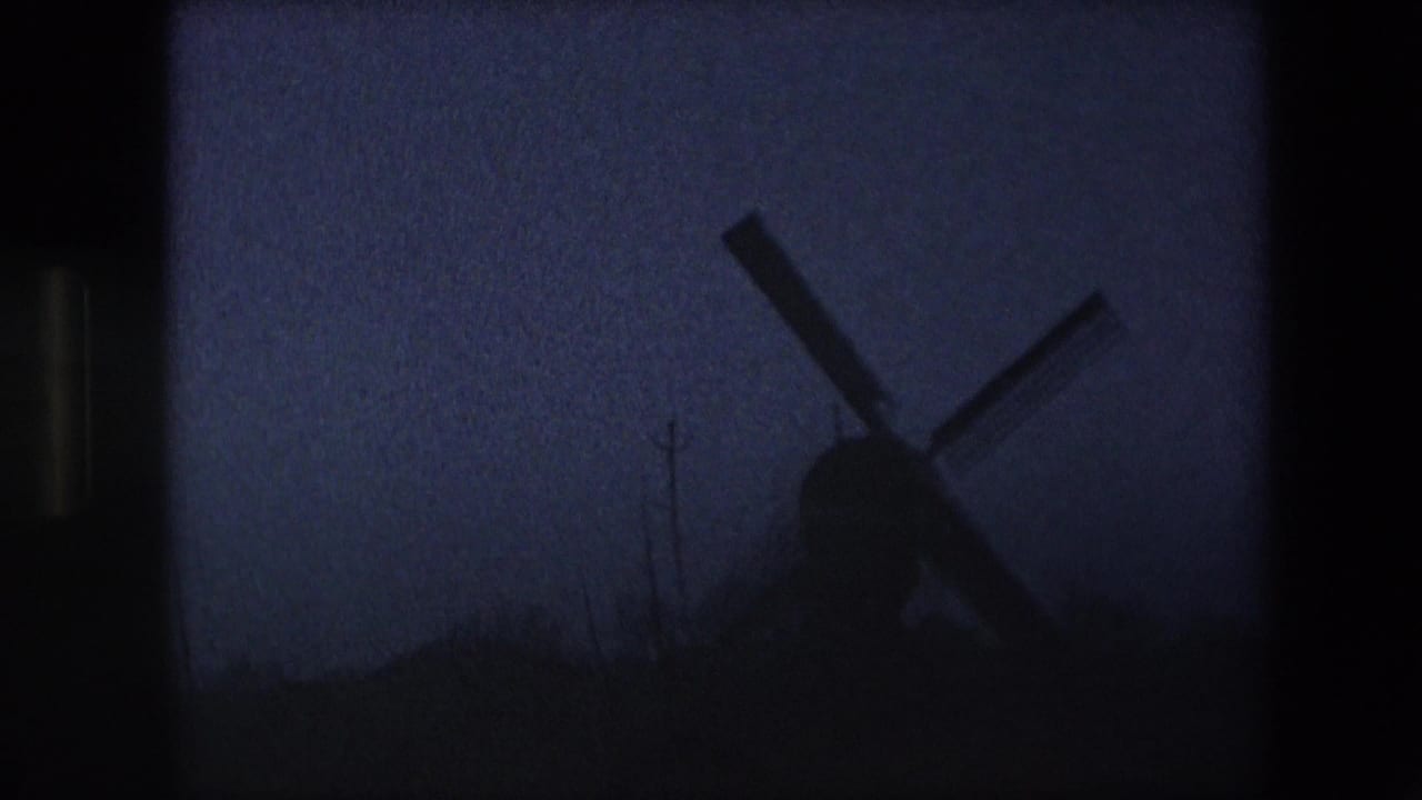 Near-dark final frame of the 1967 Brussels-area windmill shot, with the windmill reduced to a silhouette against a dim blue-purple sky and little foreground detail.