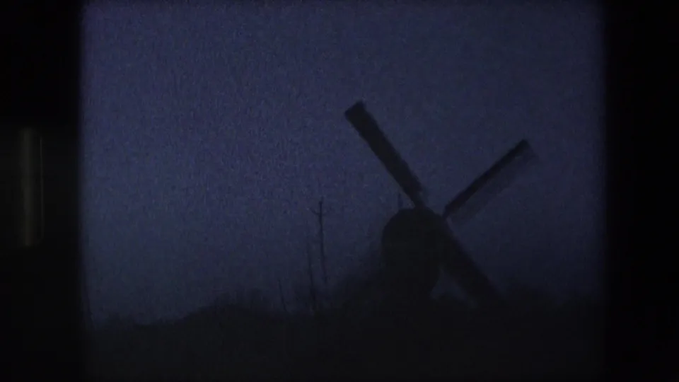 Near-dark final frame of the 1967 Brussels-area windmill shot, with the windmill reduced to a silhouette against a dim blue-purple sky and little foreground detail.