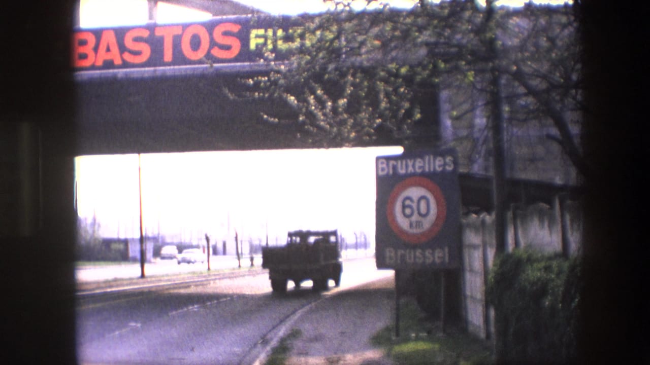 1967 Brussels road view with a truck on the highway, a bilingual Bruxelles/Brussel 60 km speed sign, and a STOS FILM advertisement above the overpass.