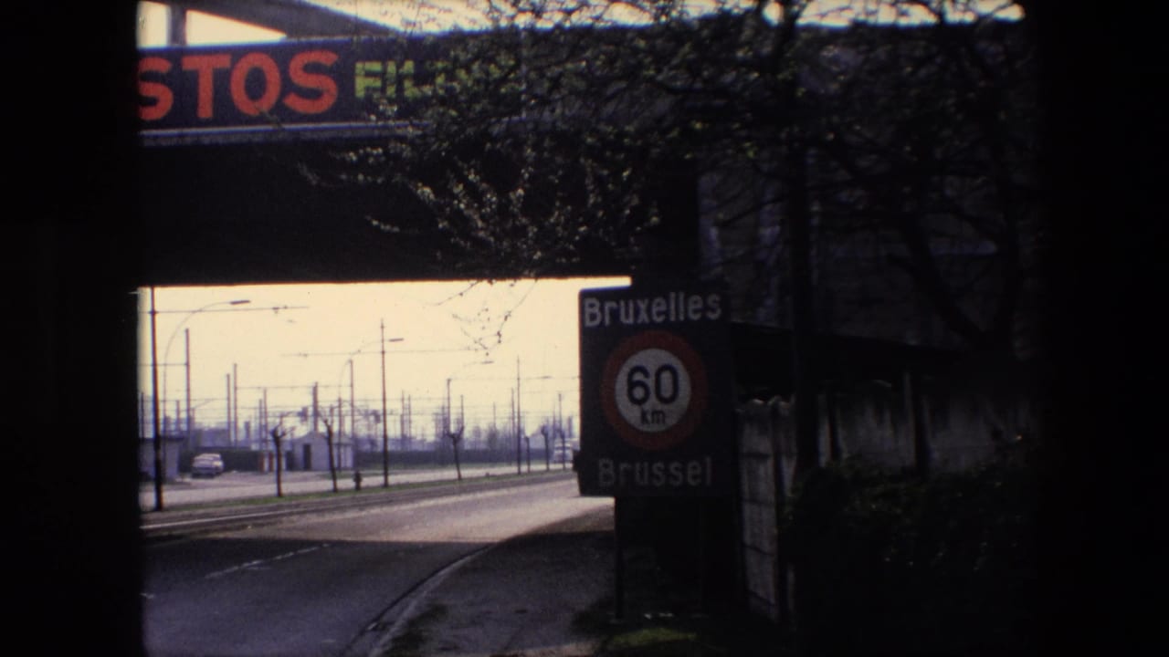 1967 Brussels highway approach beneath an overpass, showing the bilingual Bruxelles/Brussel 60 km sign, roadside poles, bare trees, and advertising on the bridge.