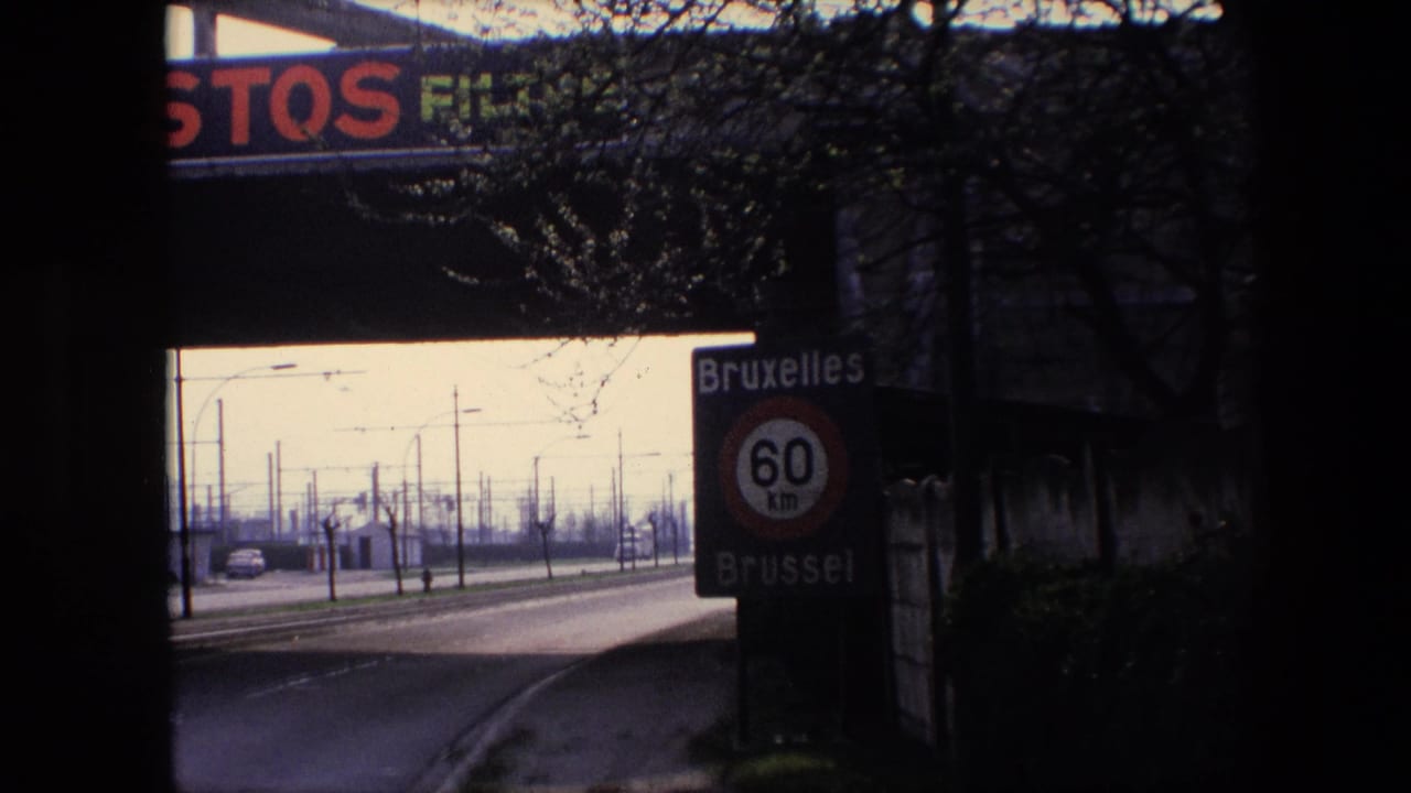 Shadowed 1967 Brussels road view with the Bruxelles/Brussel 60 km speed sign at right, open roadway at left, roadside poles, and overpass advertising above.