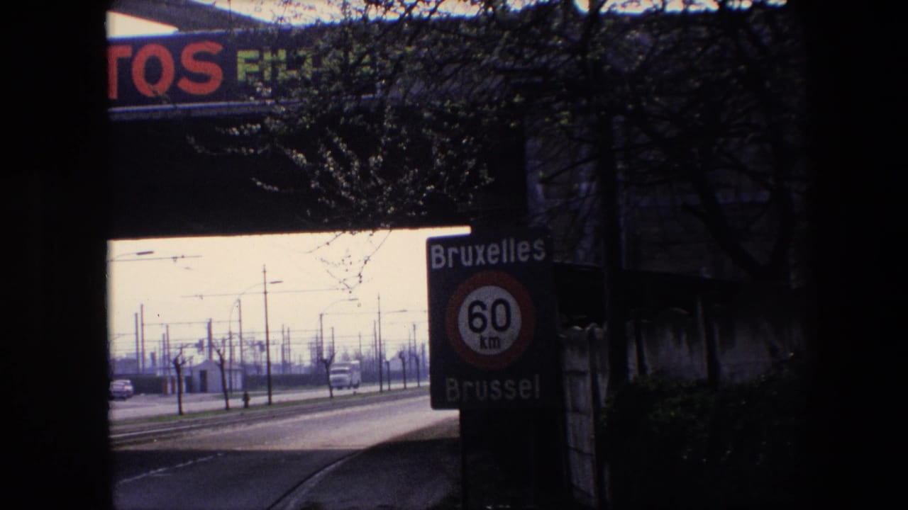 1967 Brussels highway scene with an approaching car, bilingual Bruxelles/Brussel 60 km speed sign, utility or tram poles, bare trees, and bridge advertising in frame.
