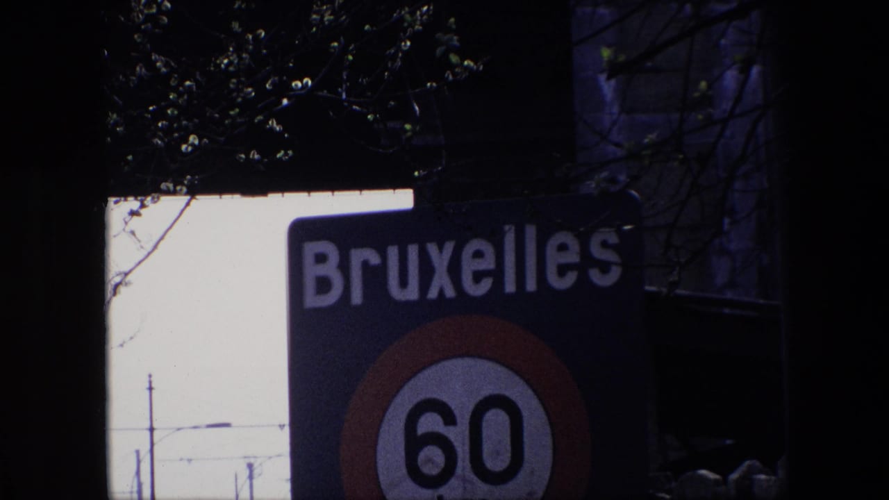 Cropped 1967 Brussels frame with the word Bruxelles visible above a partly cut off 60 km/h speed-limit sign, with branches and dark foreground shapes around it.