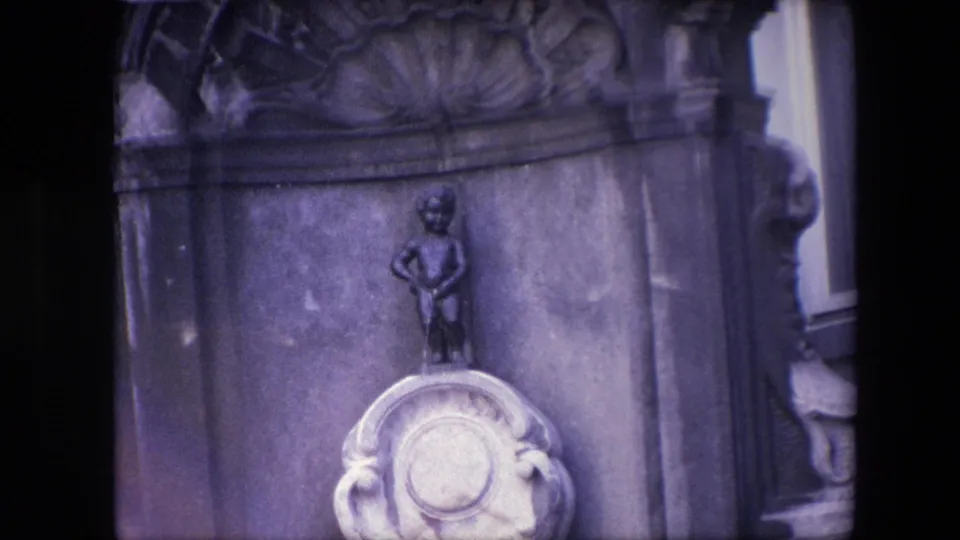 1967 Brussels 8mm frame showing the Manneken Pis figure above an ornate stone pedestal, with carved masonry and dark film borders visible.