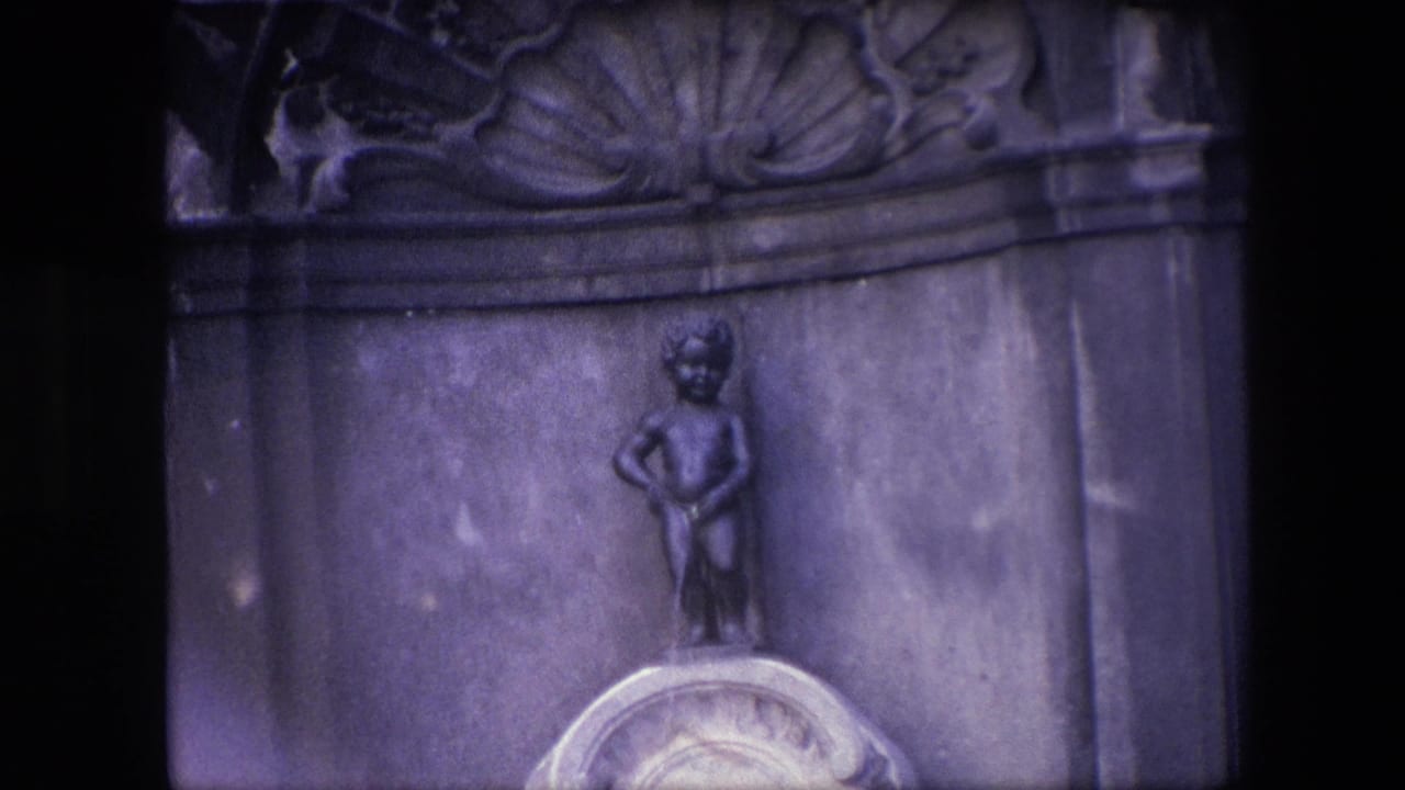 Small statue centered above a pale pedestal with carved stonework behind it.