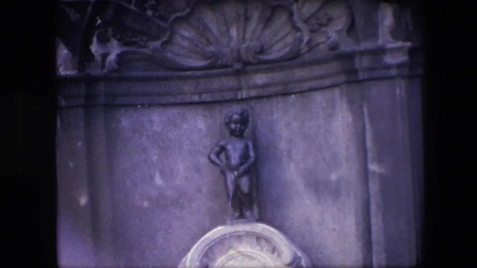 The Brussels landmark figure appears centered above the pale pedestal, framed tightly by dark edges and softened 8mm grain.