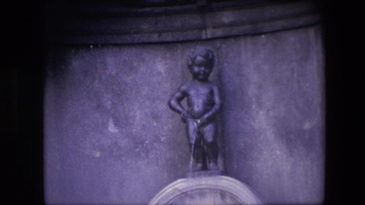 1967 Brussels 8mm frame showing the Manneken Pis fountain statue centered above a stone basin with a dark architectural background.