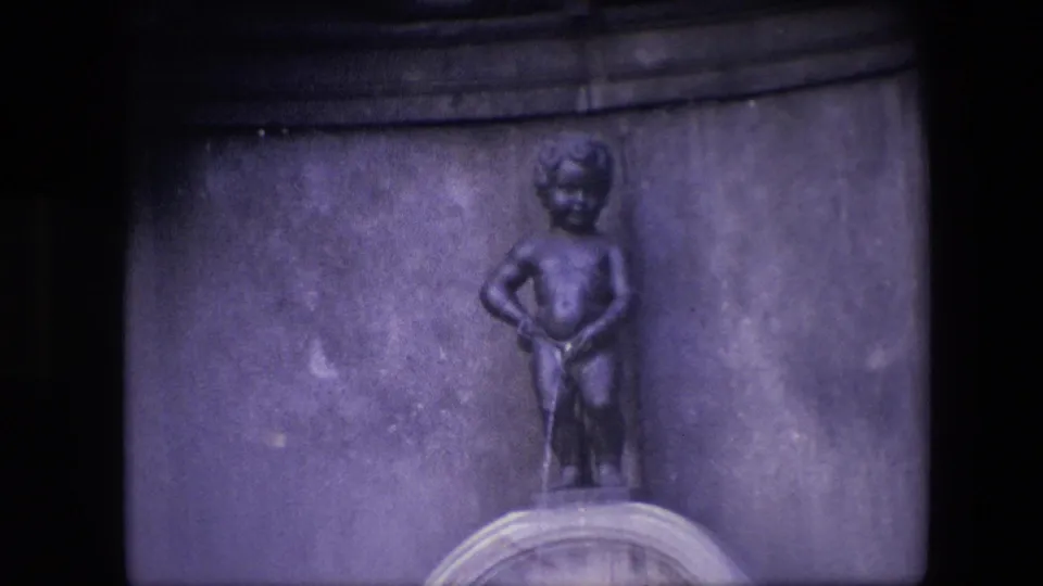 1967 Brussels 8mm frame showing the Manneken Pis fountain statue centered above a stone basin with a dark architectural background.