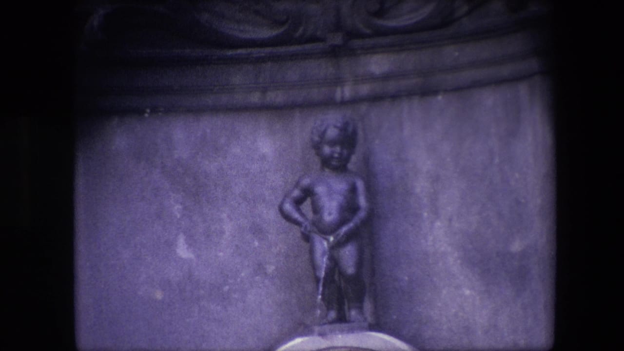 Close 1967 Brussels home-movie view of the Manneken Pis bronze figure set into a stone fountain niche with dark film borders and a purple cast.