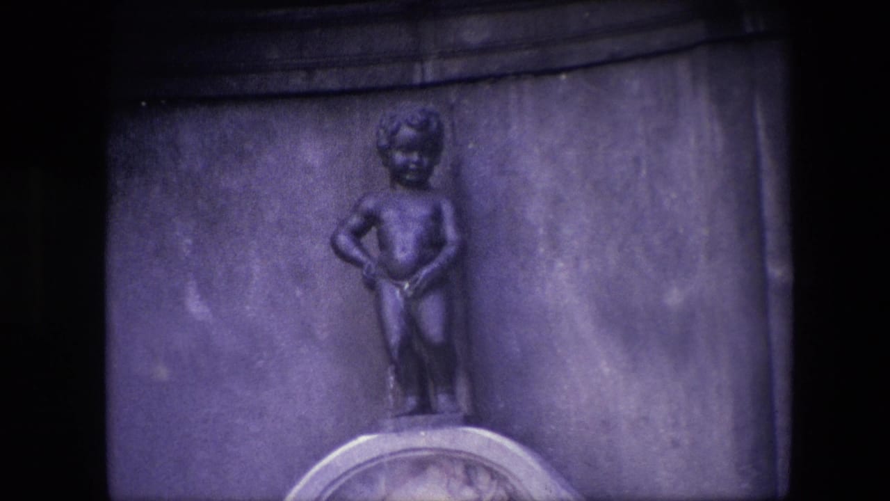 The Manneken Pis fountain figure appears centered against a broad stone backing, with the basin rim visible below in grainy 8mm color.
