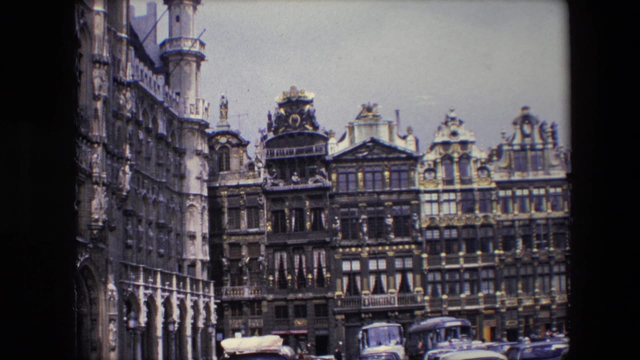 1967 Brussels 8mm frame showing ornate historic facades, arched arcades at left, parked cars, and a bus beneath an overcast sky.