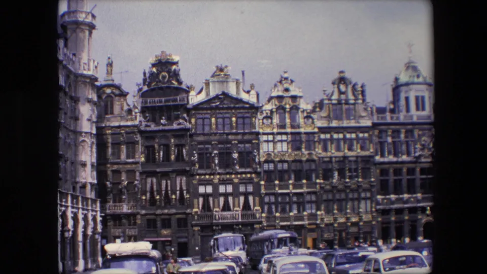 Final 1967 Brussels frame with parked cars, a bus, ornate gabled buildings, roofline details, and a rounded corner structure at the far right.