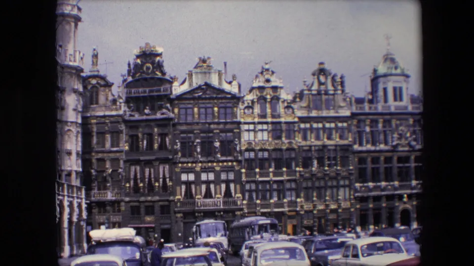 1967 8mm view of Brussels, Belgium, showing ornate Grand Place facades above parked mid-century cars and buses under an overcast sky.