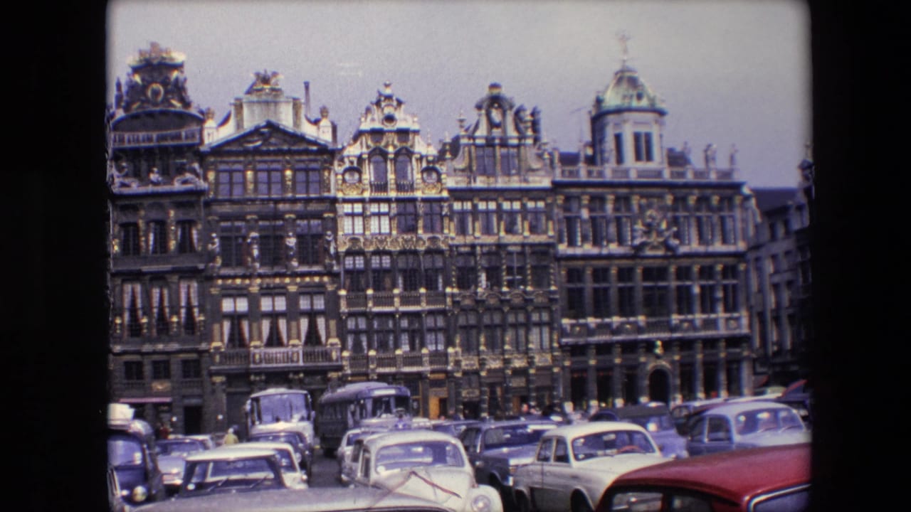 1967 Brussels street view with elaborate gabled buildings, rows of mid-century cars, and a bus or large vehicle in the foreground.