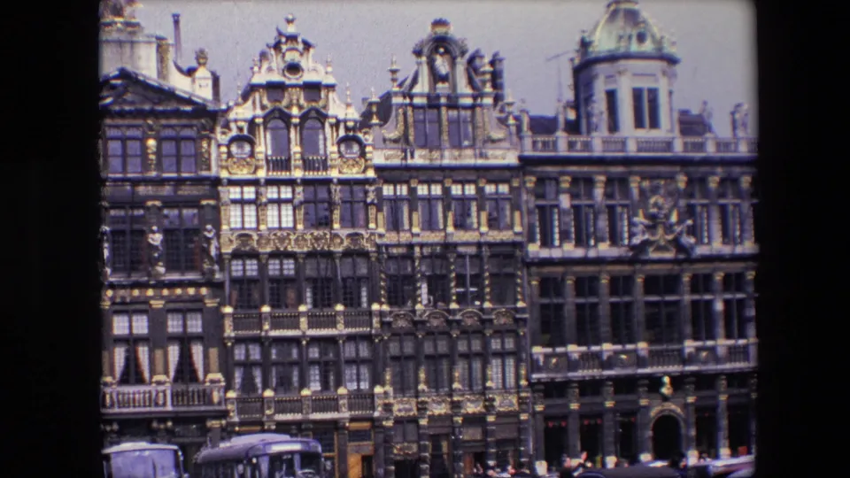 1967 Brussels home-movie frame with a slightly closer view of gilded historic facades, period cars, and small pedestrians along the street level.