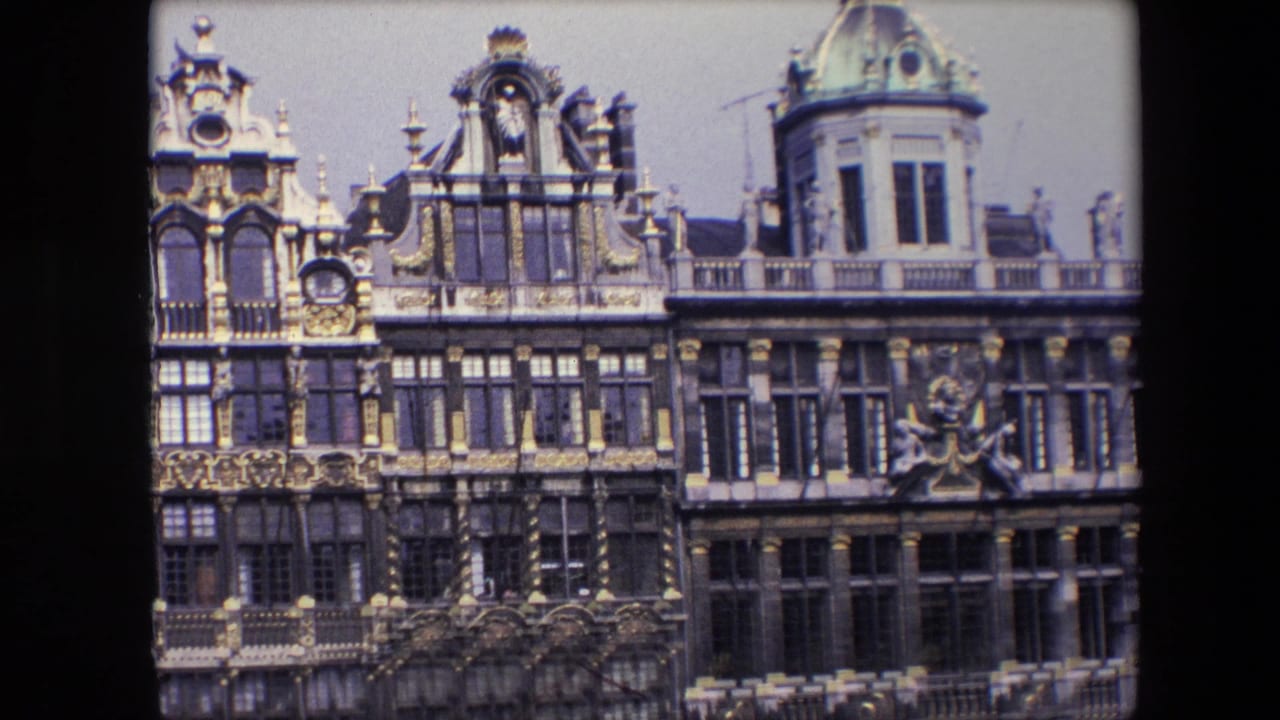 1967 Brussels home-movie frame of elaborate building fronts with gilded ornament, sculptural details, gridded windows, and a domed corner turret.