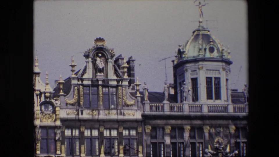 1967 Brussels visitor-shot frame showing ornate roofline details, a domed turret, sculptural facade decoration, gridded windows, and pale sky.