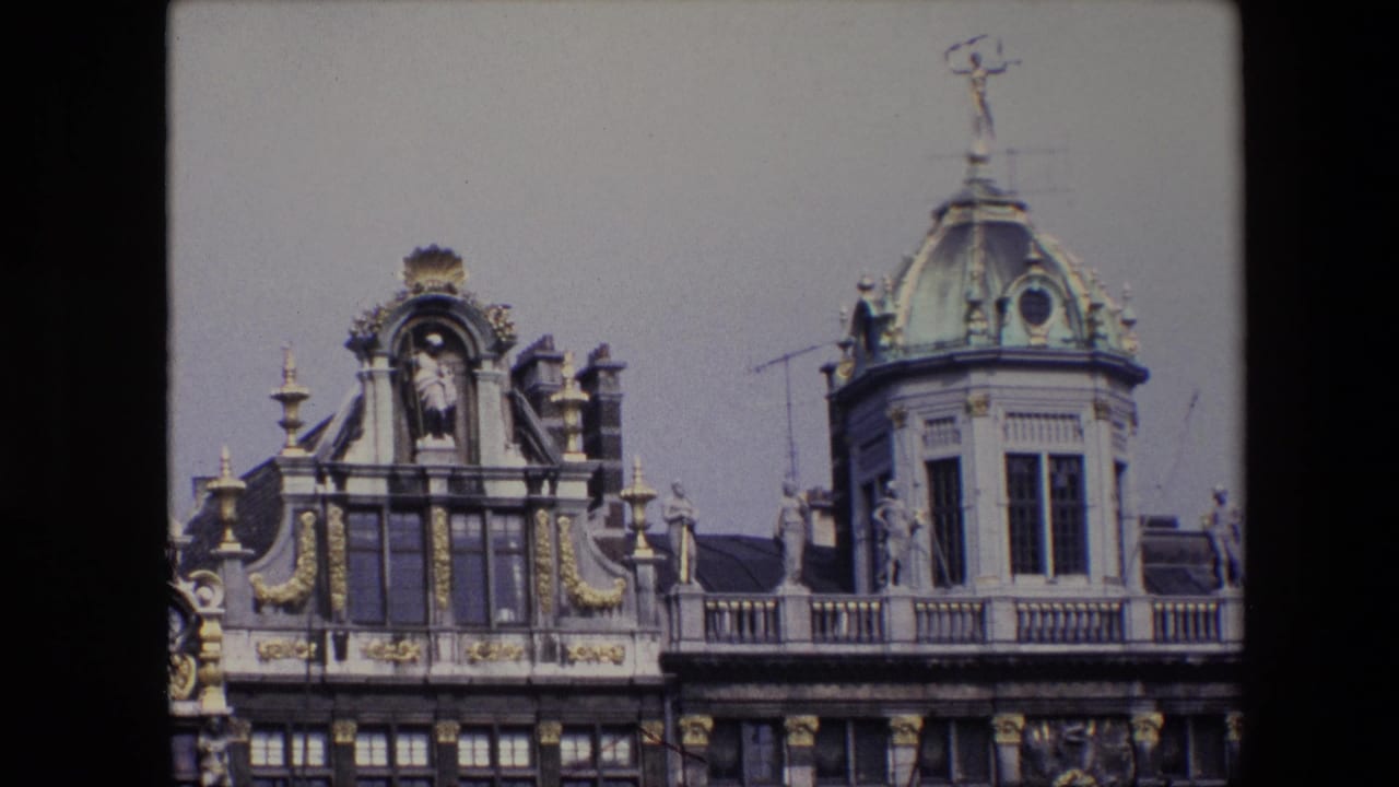 1967 Brussels 8mm frame showing an ornate building roofline with gilded decoration, classical sculptures, tall windows, antennas, and a green copper dome topped by a small statue.