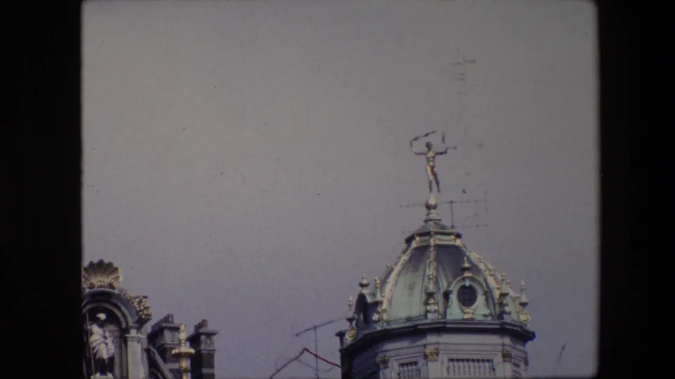 1967 Brussels 8mm frame emphasizing the green copper dome, small statue mounted above it, roof antennas, partial sculptural ornament, and pale sky.