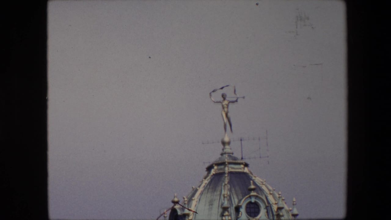 1967 Brussels 8mm frame showing a distant gilded rooftop figure on a domed copper roof with a television antenna nearby.