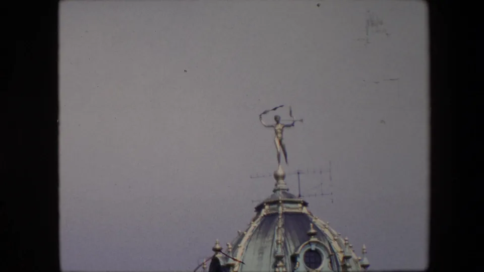 1967 Brussels 8mm frame showing a distant gilded rooftop figure on a domed copper roof with a television antenna nearby.