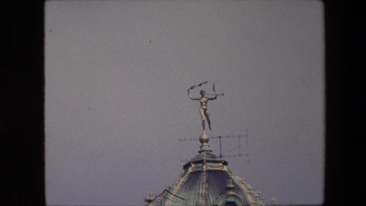 1967 Brussels frame with the rooftop statue centered high above the curved dome, seen against an open pale sky.