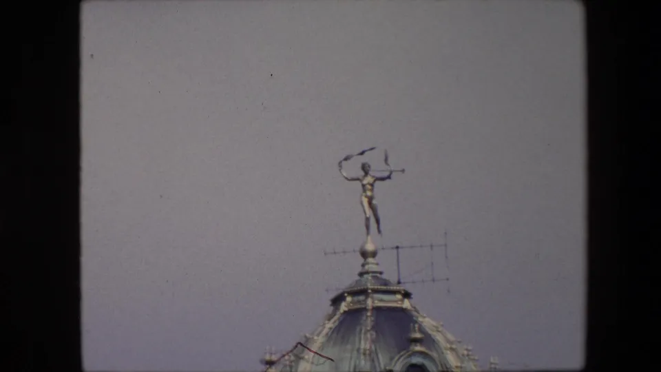 1967 Brussels frame with the rooftop statue centered high above the curved dome, seen against an open pale sky.