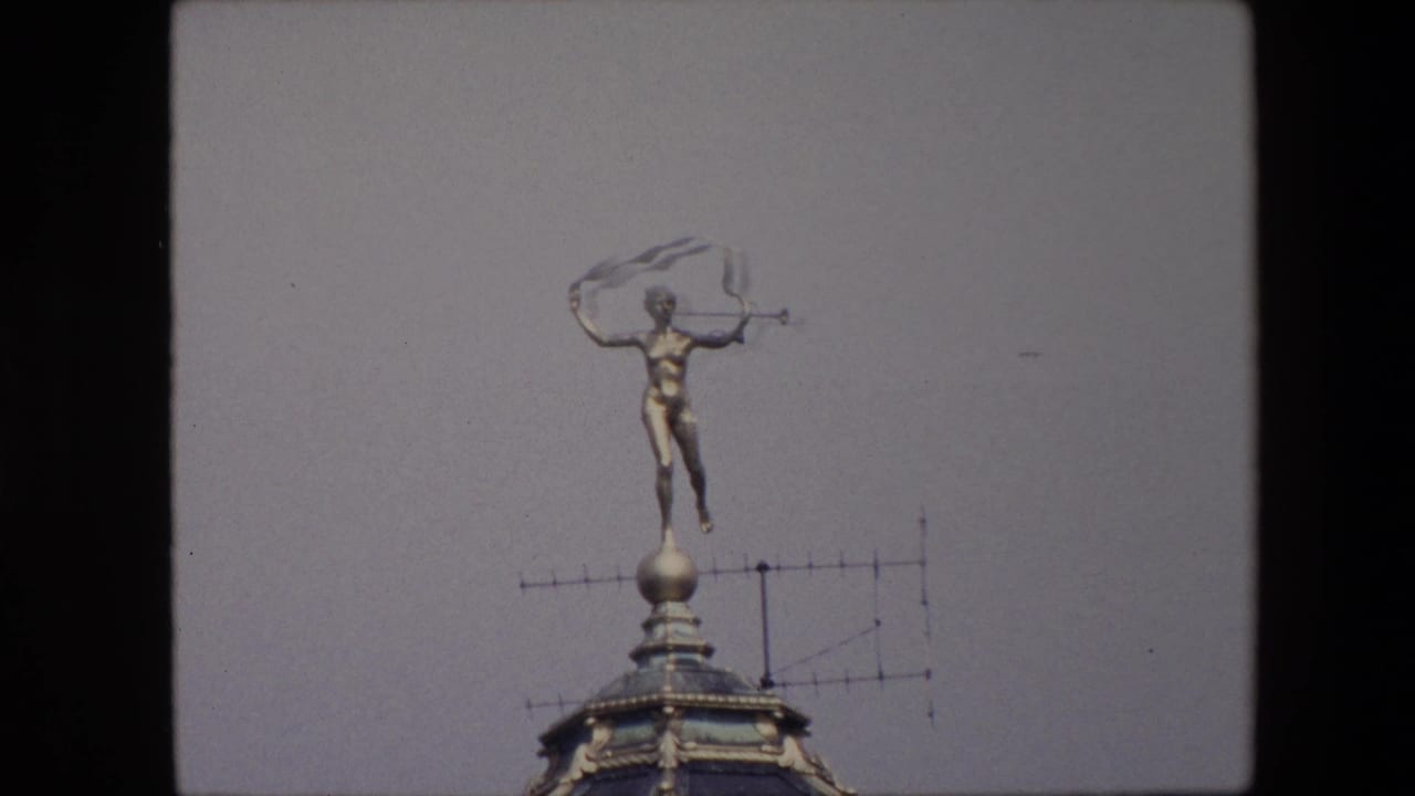 Rooftop statue with trumpet beside a television antenna on a pale sky background.