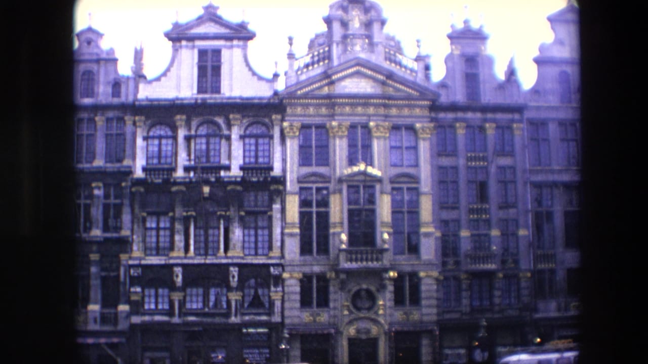 1967 Brussels 8mm frame showing ornate historic building facades with gables, columns, windows, balconies, and dark street-level shopfronts.