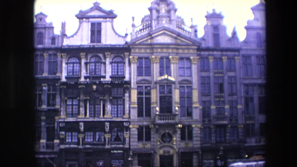 1967 Brussels 8mm frame showing ornate historic building facades with gables, columns, windows, balconies, and dark street-level shopfronts.