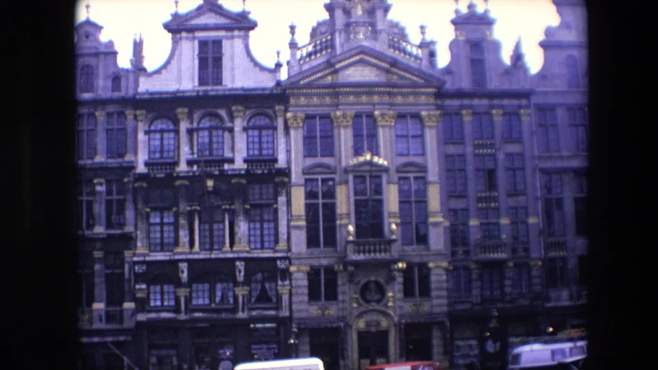 1967 Brussels 8mm frame holding on a wider view of historic multi-story facades with decorative rooflines, window rows, balconies, and a partial vehicle at the bottom edge.
