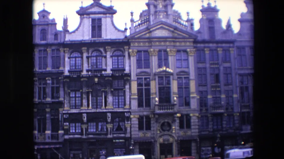 1967 Brussels 8mm frame showing an ornate building front with sculpted roofline details, repeated windows, balcony railings, and a cropped vehicle along the lower right edge.