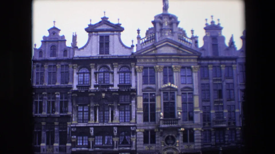 1967 Brussels home-movie still showing ornate stone facades, dark window grids and layered gables in a central urban streetscape.