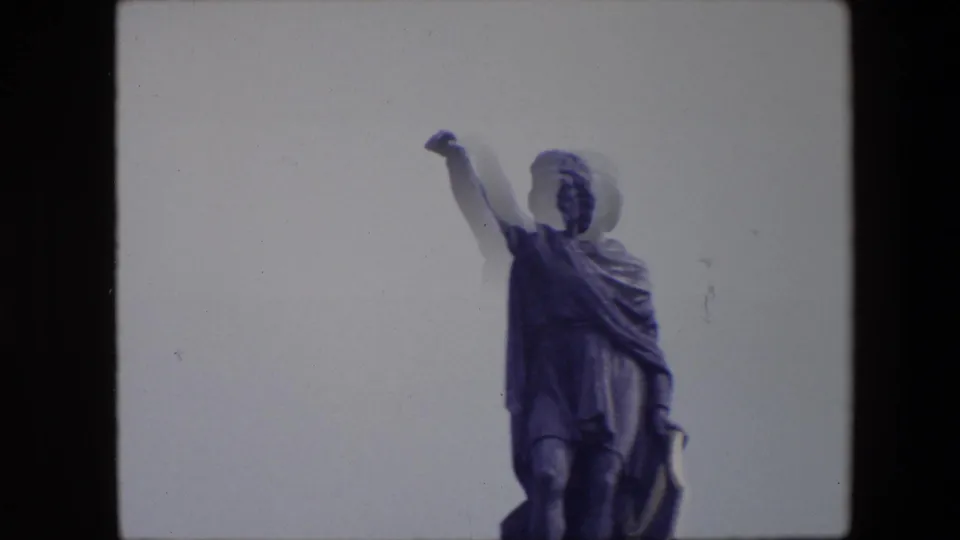 1967 Brussels 8mm frame showing a closer visitor-camera view of the robed statue, with a raised arm, cloak folds, and slight blur from camera movement.