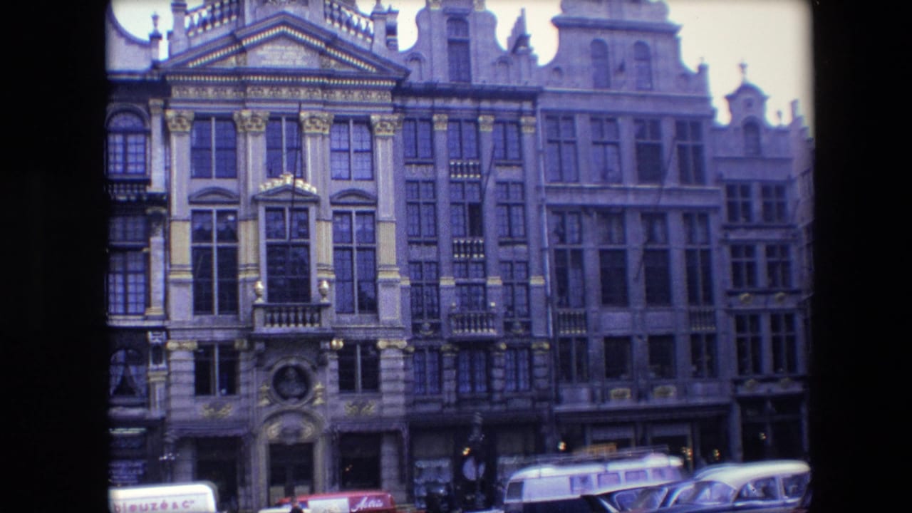 1967 Brussels street view showing ornate historic facades, decorative columns, rows of windows, partial storefront signage, and classic cars at curb level.