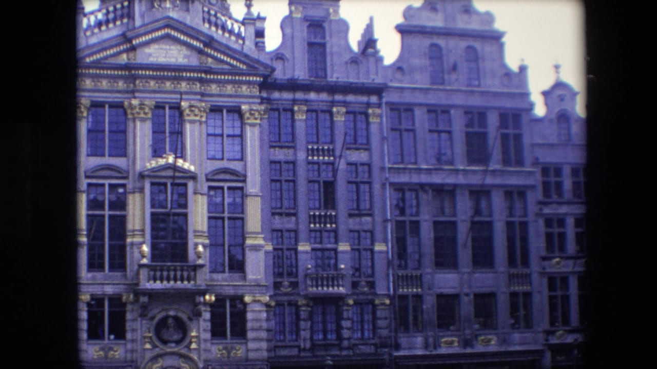 1967 Brussels footage frames a closer view of historic multi-story facades with ornate trim, tall windows, balcony details, and soft 8mm color shift.
