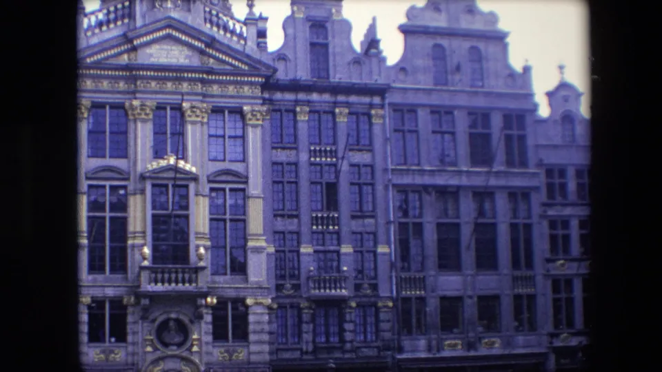 1967 Brussels footage frames a closer view of historic multi-story facades with ornate trim, tall windows, balcony details, and soft 8mm color shift.