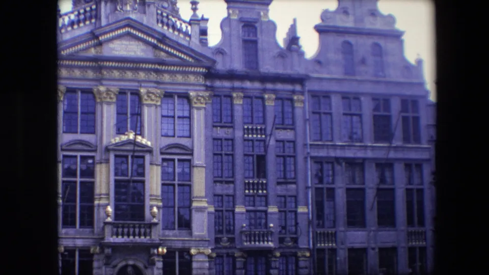 The zoom brings the Brussels facades nearer, emphasizing carved stonework, window grids, small balconies, and the soft purple cast of the scanned 8mm film.